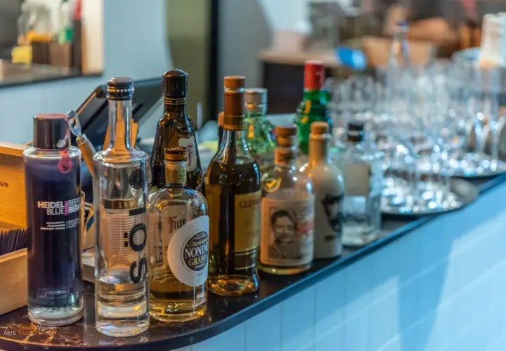 Eine Auswahl an Flaschen, darunter eine blaue Heidelbeer-Wodka-Flasche, steht auf einer Bar. Was ist Wodka? Eine klare Spirituose, oft aus Getreide oder Kartoffeln hergestellt.