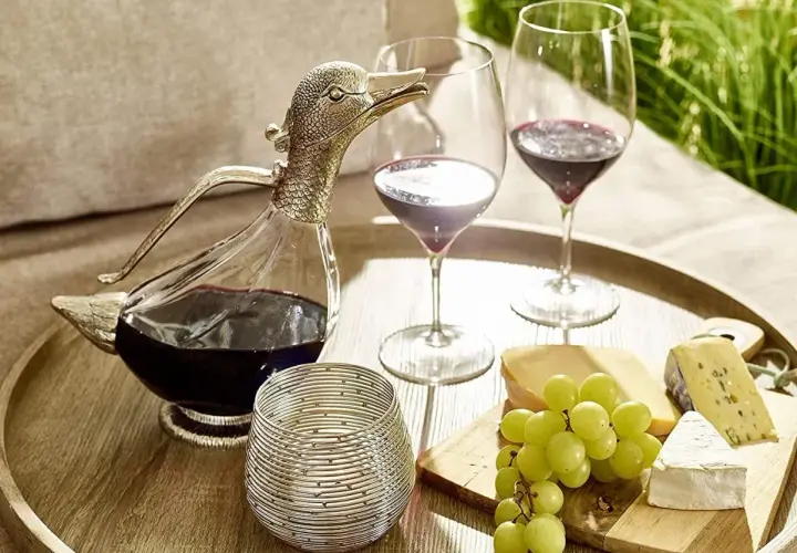 Ein Entenschnabel-Dekanter mit Rotwein, zwei Weingläser, Käse und Trauben auf einem Tablett – so gelingt das Wein richtig einschenken.
