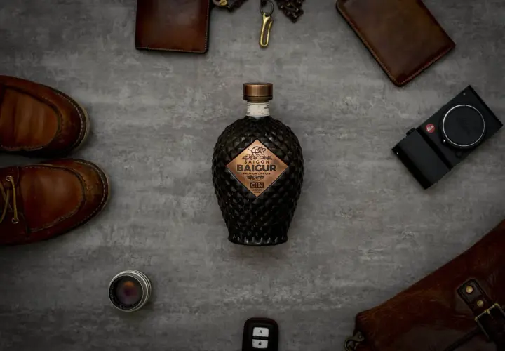 Edle Flasche Saigon Baigur Gin mit 43% Alkohol, umgeben von Lederaccessoires und einer Leica Kamera.