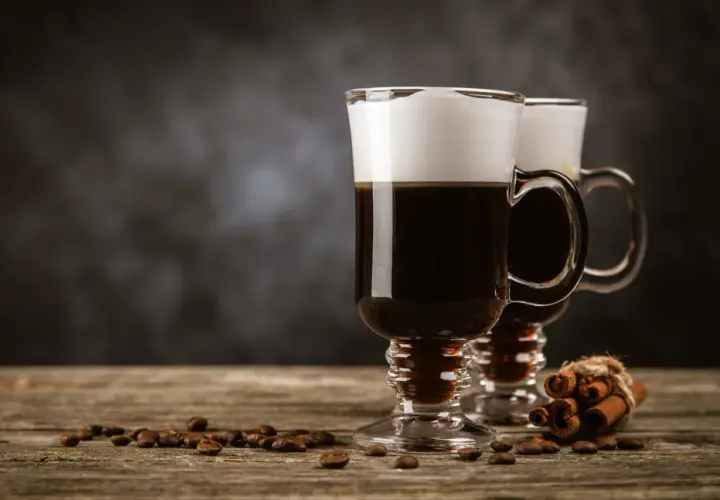 Zwei Irish Coffee Gläser mit Sahnehaube, Kaffeebohnen und Zimtstangen. Perfekt für Irish Coffee Rezepte.