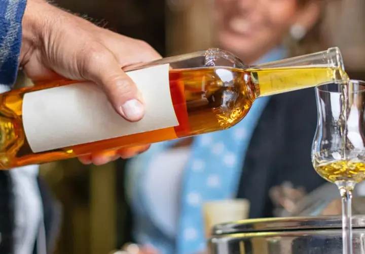 Ein Mann gießt goldbraunen Grappa in ein Glas. So trinkt man Grappa kalt, ein Genuss für besondere Momente.