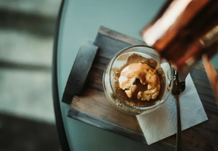 Ein Affogato: heißer Espresso fließt über eine Kugel cremiges cafe eis. Ein Löffel liegt daneben.