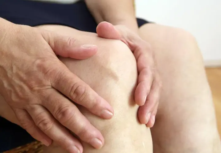 Hände umfassen ein schmerzendes Knie. Mögliche Ursache: Sulfite im Wein können Gelenkschmerzen verstärken.