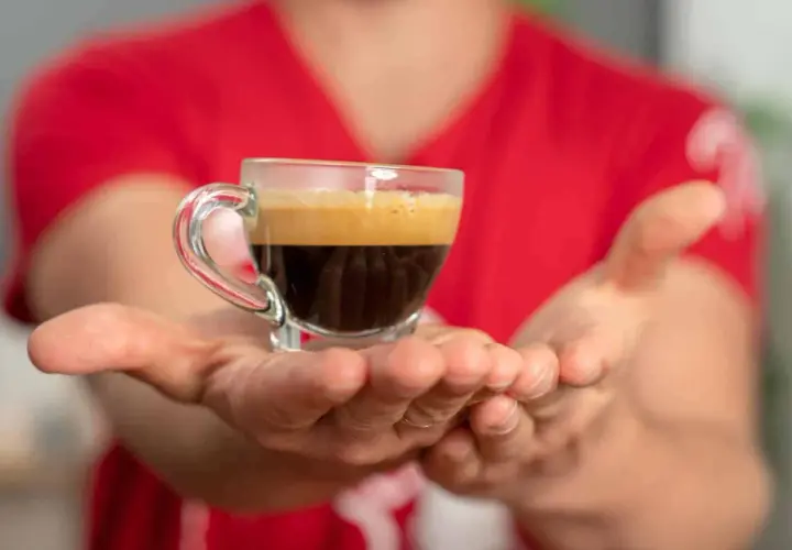Hände reichen eine kleine Tasse Espresso, bereit für einen belebenden Kaffee-Nap.