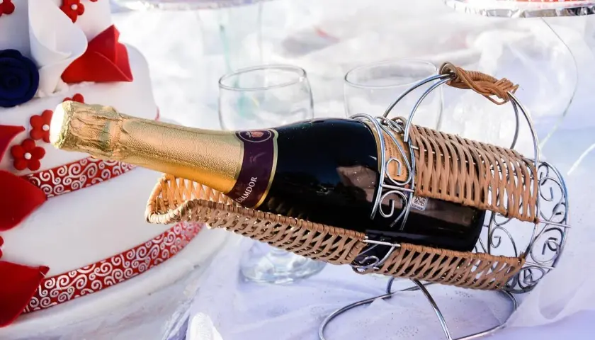 Sektflasche in einem Weidenkorb, neben einer Hochzeitstorte. Das Wein-Ablaufdatum ist hier unwichtig, die Freude zählt.