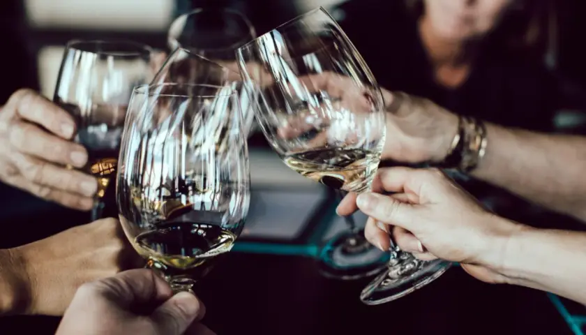Hände halten Weingläser am Stiel, um den Wein richtig zu halten. Ein Toast wird ausgesprochen.