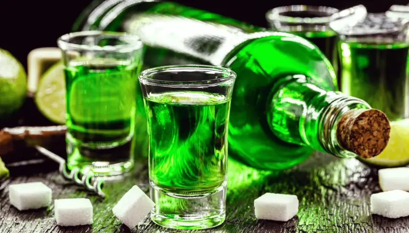 Grüner Branntwein aus Wermut, serviert in Schnapsgläsern mit Zuckerwürfeln und Limettenspalten.