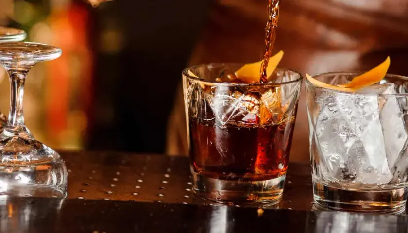Ein dunkler Whisky wird in ein Glas mit Eis und Orangenzeste gegossen. So trinkt man Whisky.