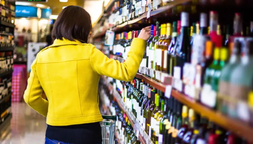 Frau in gelber Jacke wählt Wein aus dem Regal, um die beste **Wein-Bewertung** zu finden.