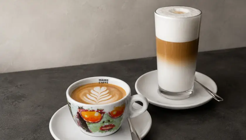 Zwei Kaffeespezialitäten: ein Cappuccino in einer bunten Tasse und ein Latte Macchiato im Glas. Die Frage "wie viel espresso in cappuccino" wird hier visuell beantwortet.