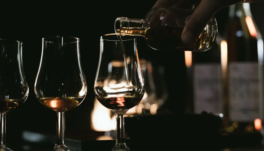 Ein Glas wird mit bernsteinfarbenem Brandy oder Cognac gefüllt, während andere Gläser bereitstehen.