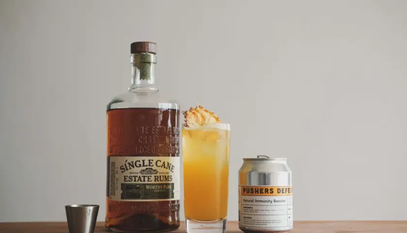 Flasche Single Cane Estate Rums, ein Cocktail mit Ananas und eine Dose "Pushers Defense". Der Rum hat seine Herkunft auf Jamaika.