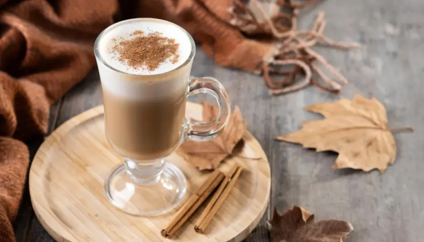 Ein warmer Herbst Kaffee mit Zimt, umgeben von Blättern und einer kuscheligen Decke.