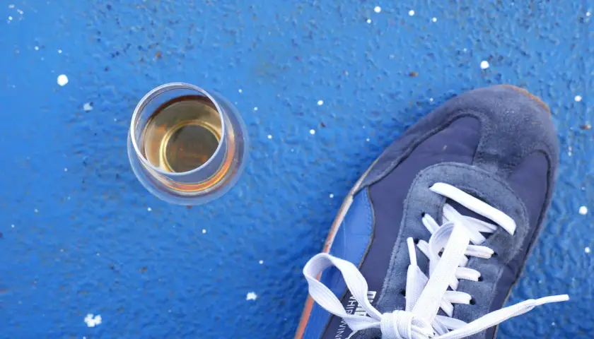 Ein Glas Whisky steht neben einem blauen Sneaker. Wer sich fragt, wie viel Kalorien hat Whisky, findet hier eine visuelle Anregung.