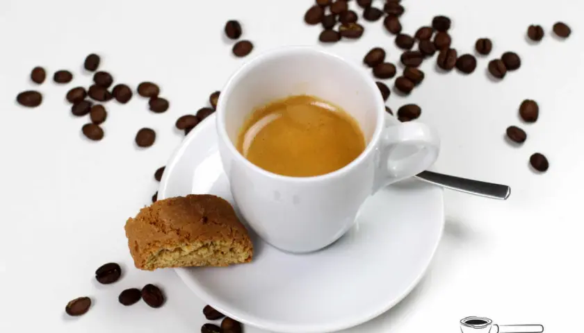 Ein cremiger Espresso Lungo in weißer Tasse, daneben ein Cantuccini und Kaffeebohnen.