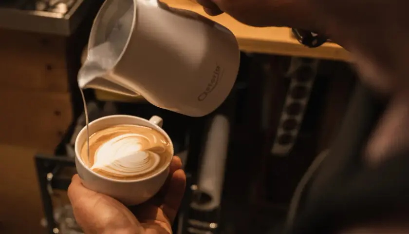 Barista verziert einen Kaffee mit kunstvoller cafe latte art. Ein Herz aus Milchschaum entsteht.