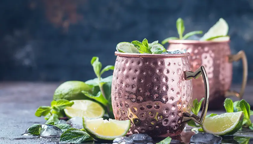 Zwei eisgekühlte Moscow Mule Becher mit Limette und Minze. Die Herkunft des Moscow Mule ist eine interessante Geschichte.