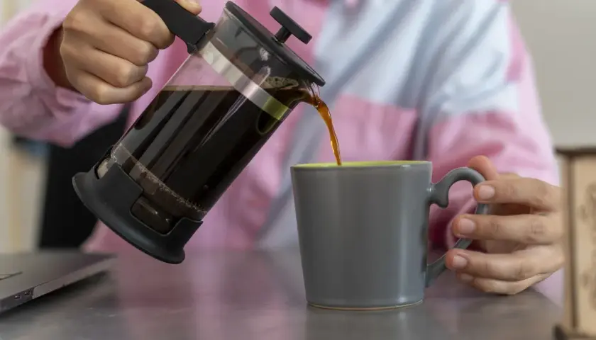 Kaffee wird aus einer French Press in eine graue Tasse gegossen.