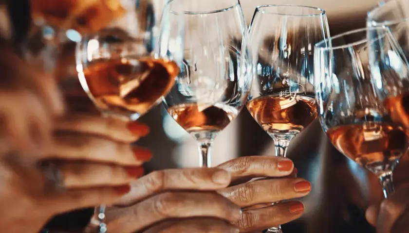 Hände halten Gläser mit Roséwein. Die Frage, warum Sulfite im Wein sind, beschäftigt viele Genießer.