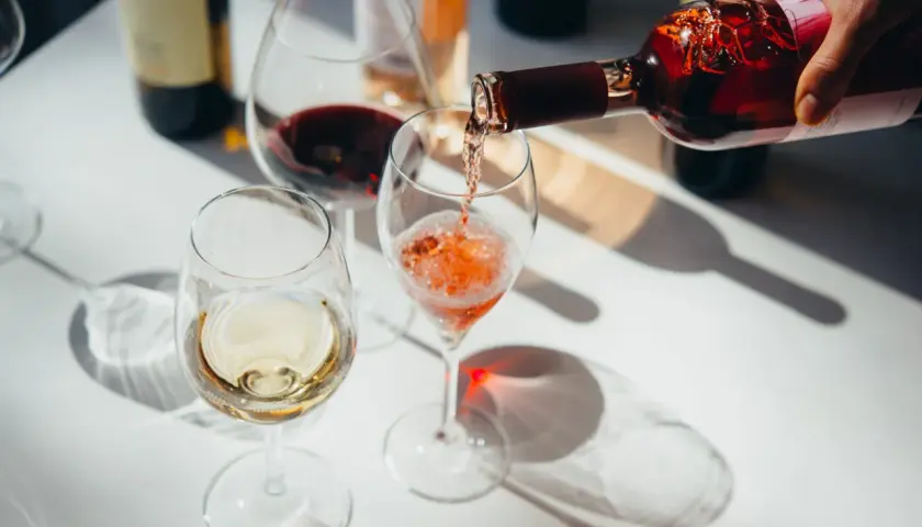 Roséwein wird in ein Glas gegossen, während Weiß- und Rotwein bereits in anderen Gläsern stehen. Ein schöner Moment, um Wein zu servieren.