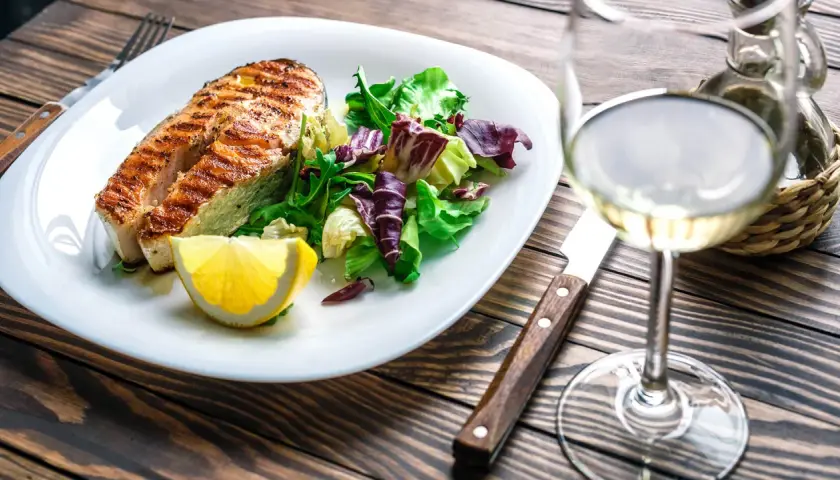 Gegrilltes Lachsfilet mit Salat und Zitrone, dazu ein Glas Weißwein, der den Riesling Geschmack unterstreicht.