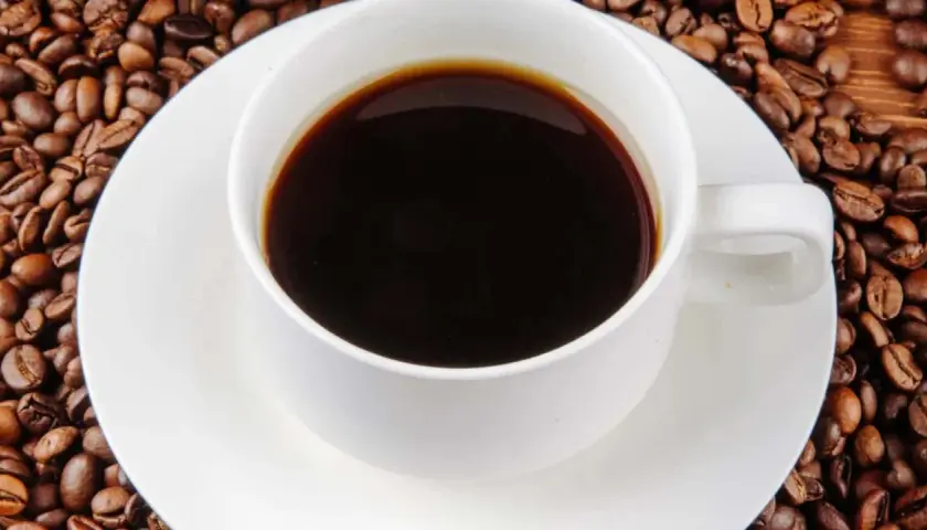Eine Tasse schwarzer Kaffee umgeben von gerösteten Kaffeebohnen. Die Frage "wie viel Koffein hat Kaffee?" wird durch dieses Bild aufgeworfen.