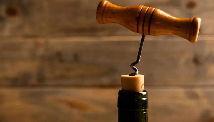 Ein Holzkorkenzieher mit Metallspirale wird in einen Korken gedreht. So funktioniert ein Korkenzieher: Drehen, bis die Spirale greift, dann ziehen.