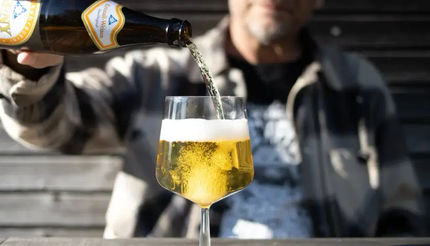Ein Mann gießt ein Kristall-Weizenbier in ein Glas. Die Flasche zeigt "0,33l". Wenige Kalorien für diesen Genuss.