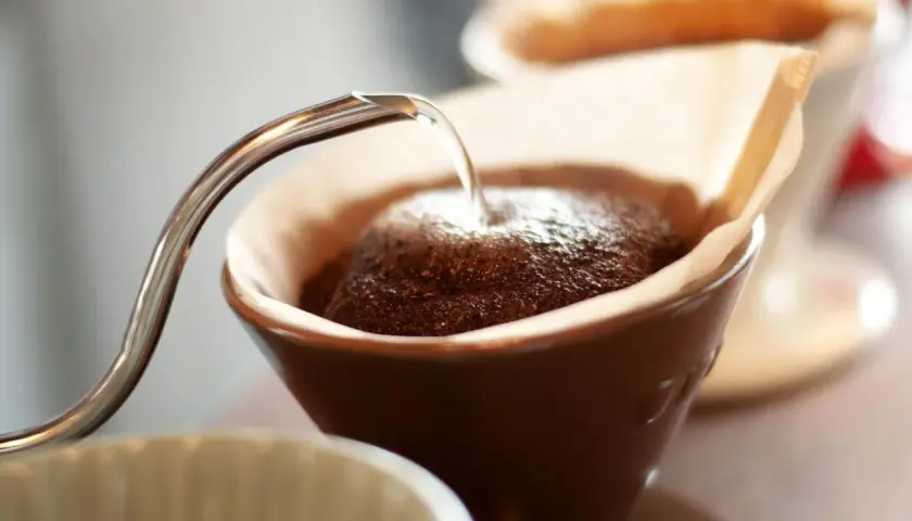 Heißes Wasser fließt aus einer schmalen Kanne auf frisch gemahlenen Kaffee in einem Filter. Der Prozess des Kaffee filterns beginnt.