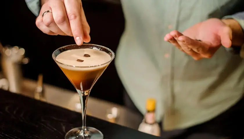 Ein Barkeeper garniert einen Espresso-Martini mit Kaffeebohnen. Dieser Kaffee Cocktail ist ein Genuss.