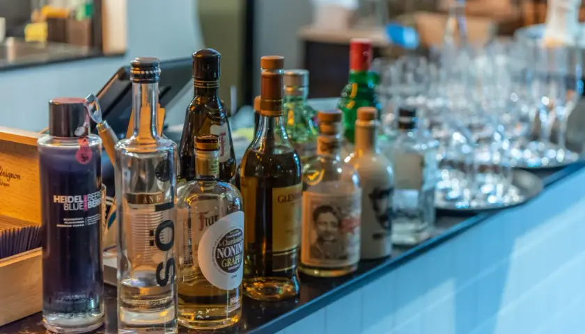 Eine Auswahl an Flaschen, darunter eine blaue Heidelbeer-Wodka-Flasche, steht auf einer Bar. Was ist Wodka? Eine klare Spirituose, oft aus Getreide oder Kartoffeln hergestellt.