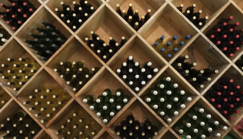 Holzregal mit vielen Flaschen Wein, ideal zum rotwein lagern. Verschiedene Sorten und Farben sind zu sehen.