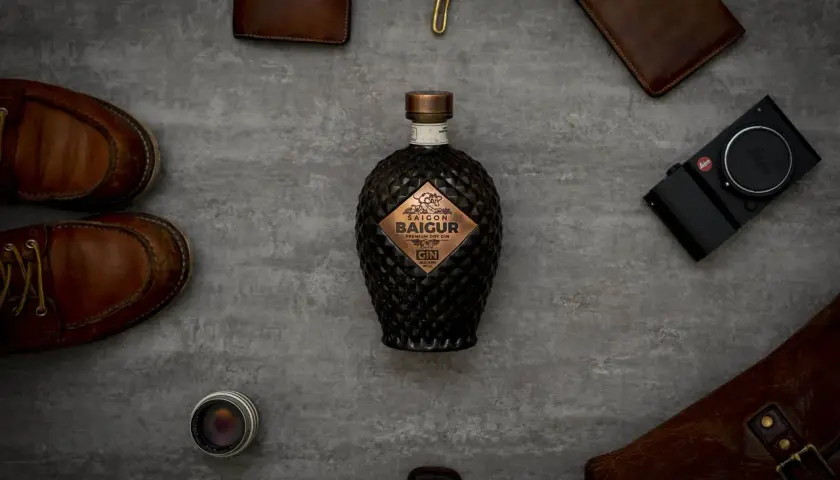 Edle Flasche Saigon Baigur Gin mit 43% Alkohol, umgeben von Lederaccessoires und einer Leica Kamera.