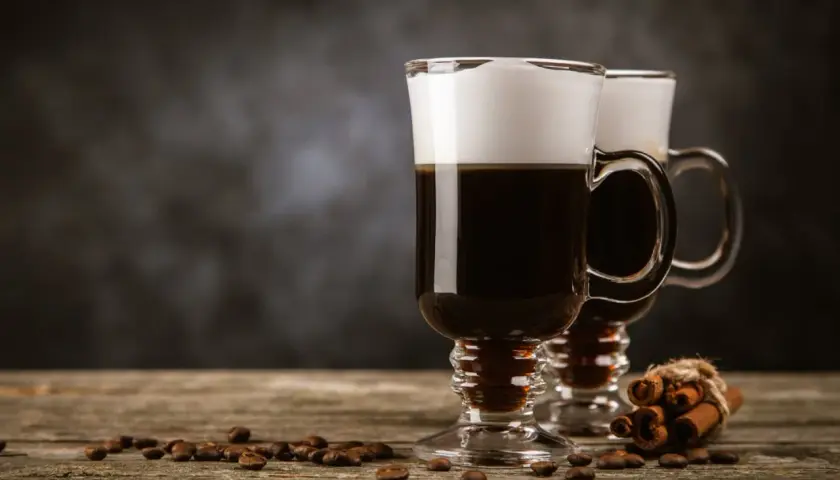 Zwei Irish Coffee Gläser mit Sahnehaube, Kaffeebohnen und Zimtstangen. Perfekt für Irish Coffee Rezepte.
