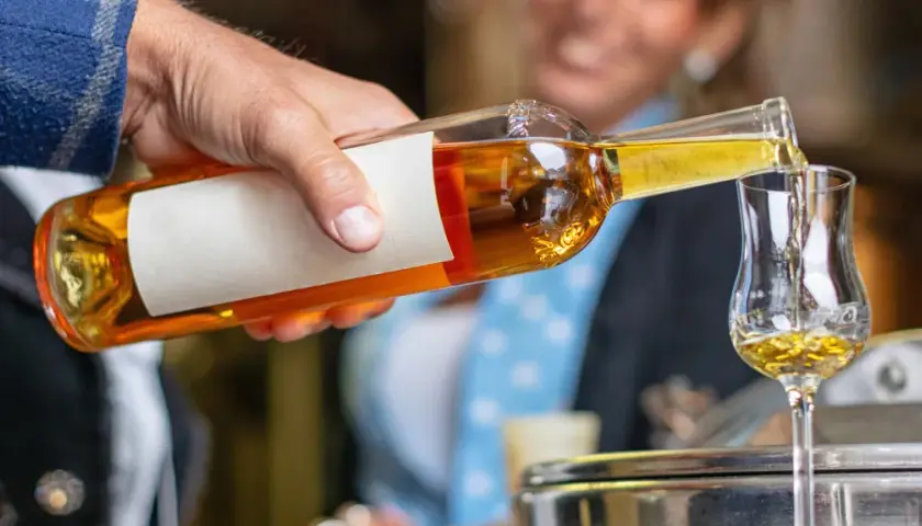 Ein Mann gießt goldbraunen Grappa in ein Glas. So trinkt man Grappa kalt, ein Genuss für besondere Momente.
