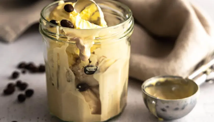 Cremiges Kaffee-Eis im Glas, perfekt für ein schnelles Rezept. Ein Löffel hebt das köstliche Eis hervor, umgeben von Kaffeebohnen.