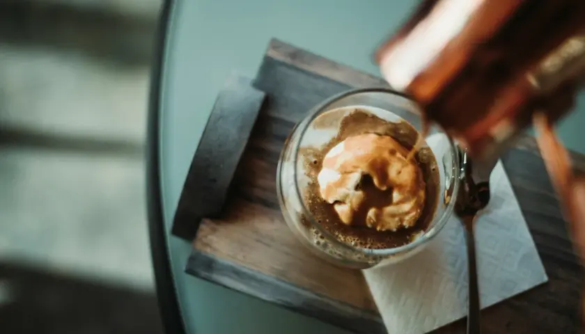 Ein Affogato: heißer Espresso fließt über eine Kugel cremiges cafe eis. Ein Löffel liegt daneben.