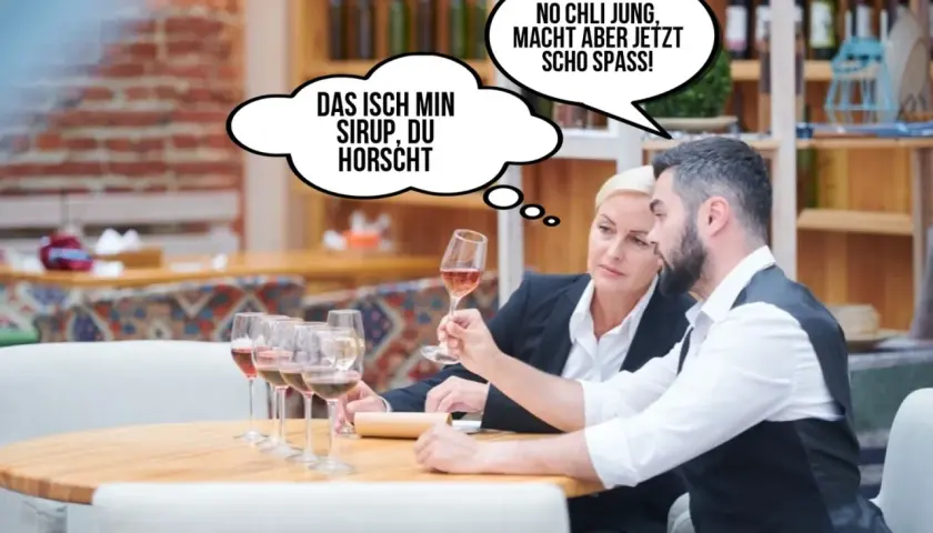 Zwei Personen probieren Wein. Eine denkt: "Das isch min Sirup, du horscht." Die andere: "No chli jung, macht aber jetz scho spass!" Lustig, wie sie den Wein beschreiben.
