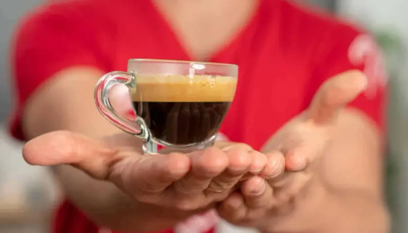 Hände reichen eine kleine Tasse Espresso, bereit für einen belebenden Kaffee-Nap.