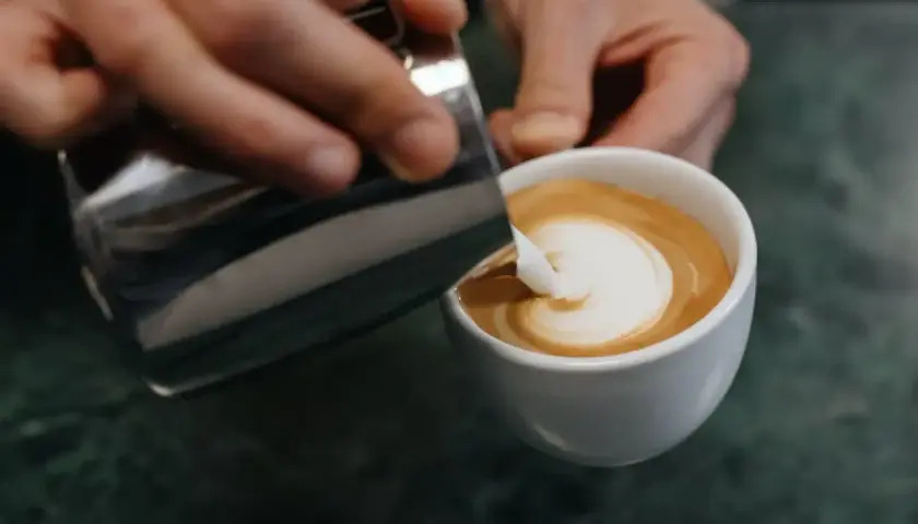 Barista zaubert mit Milch und Espresso ein Herz in die Tasse – ein Meisterwerk der Barista Art.