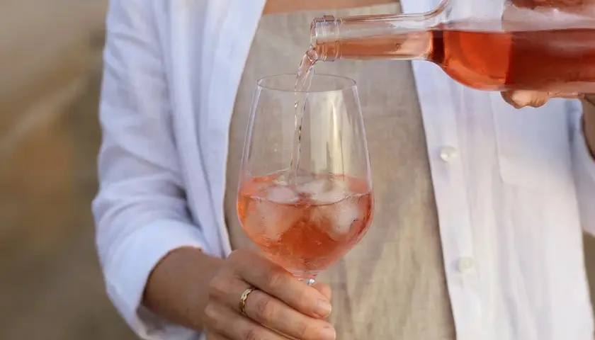Eine Person schenkt Roséwein mit Eiswürfeln in ein Glas. Die ideale rosewein temperatur für diesen erfrischenden Genuss.