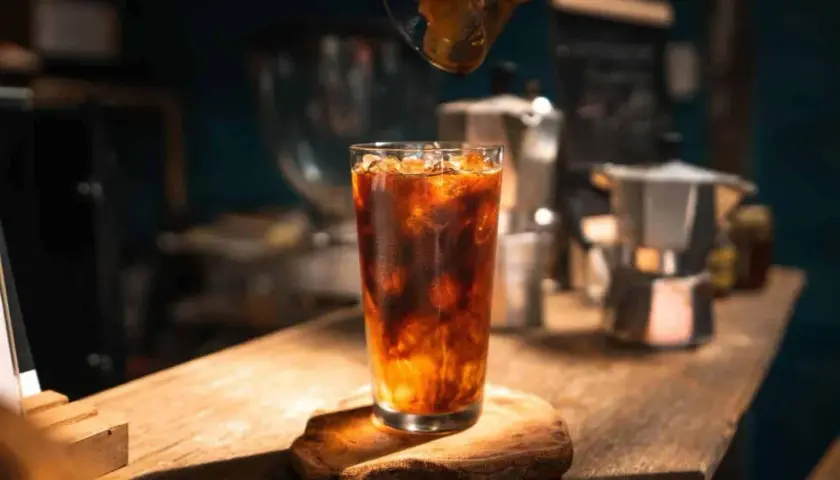 Ein erfrischender Eis Americano wird zubereitet, während Espresso in das Glas mit Eis und Wasser gegossen wird.