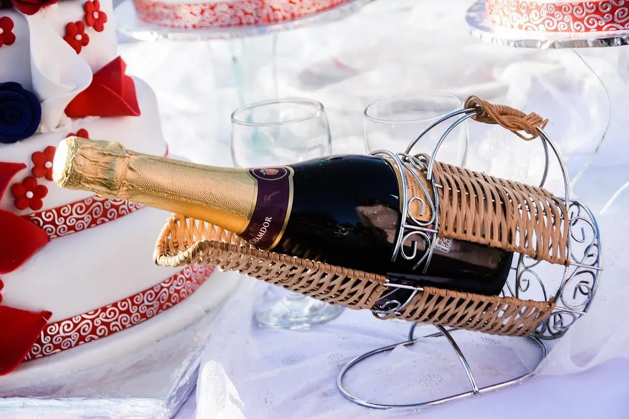 Sektflasche in einem Weidenkorb, neben einer Hochzeitstorte. Das Wein-Ablaufdatum ist hier unwichtig, die Freude zählt.