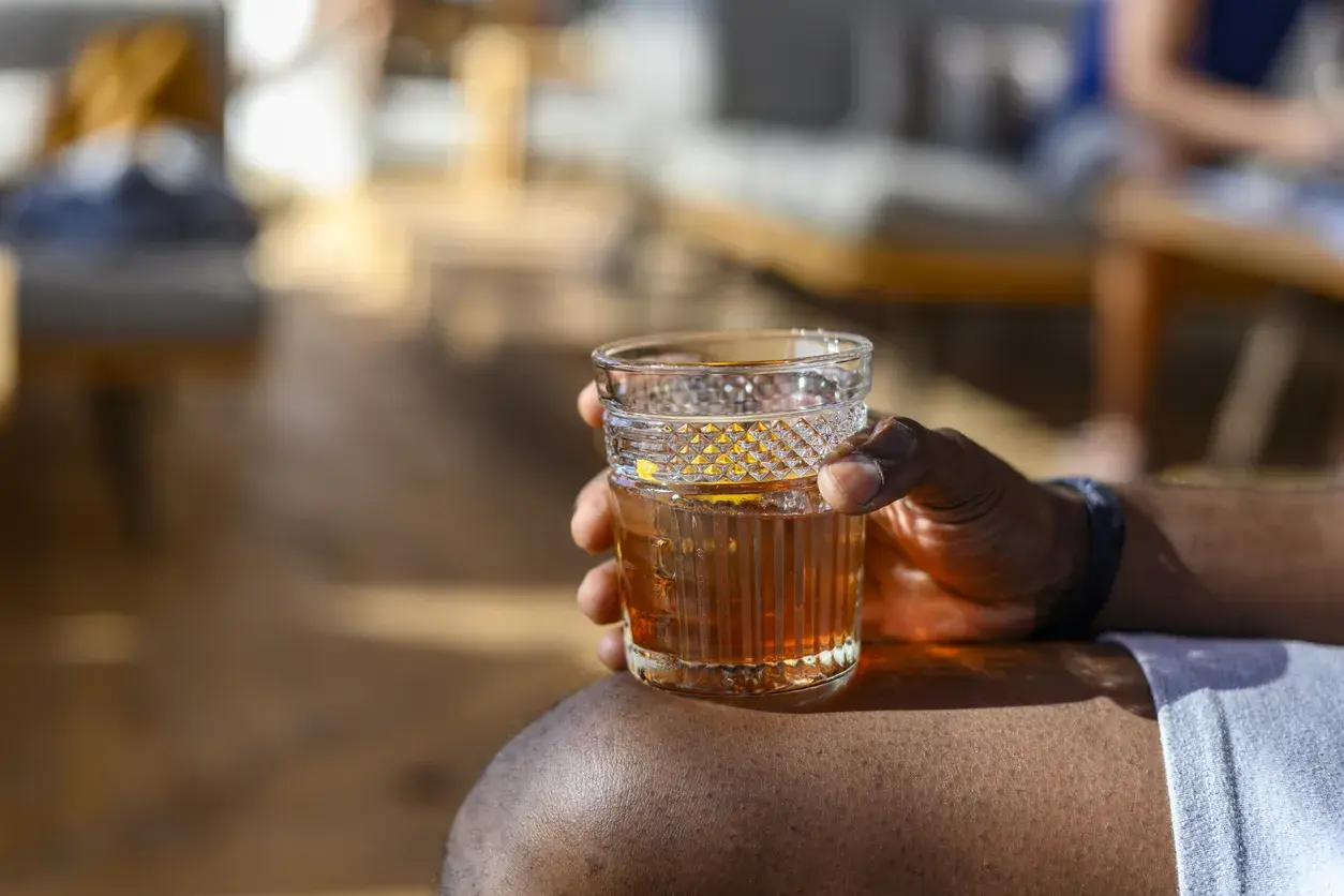 Ein Mann hält ein Glas Wermut mit Eis und Orangenzeste. So trinkt man Wermut an einem sonnigen Tag.