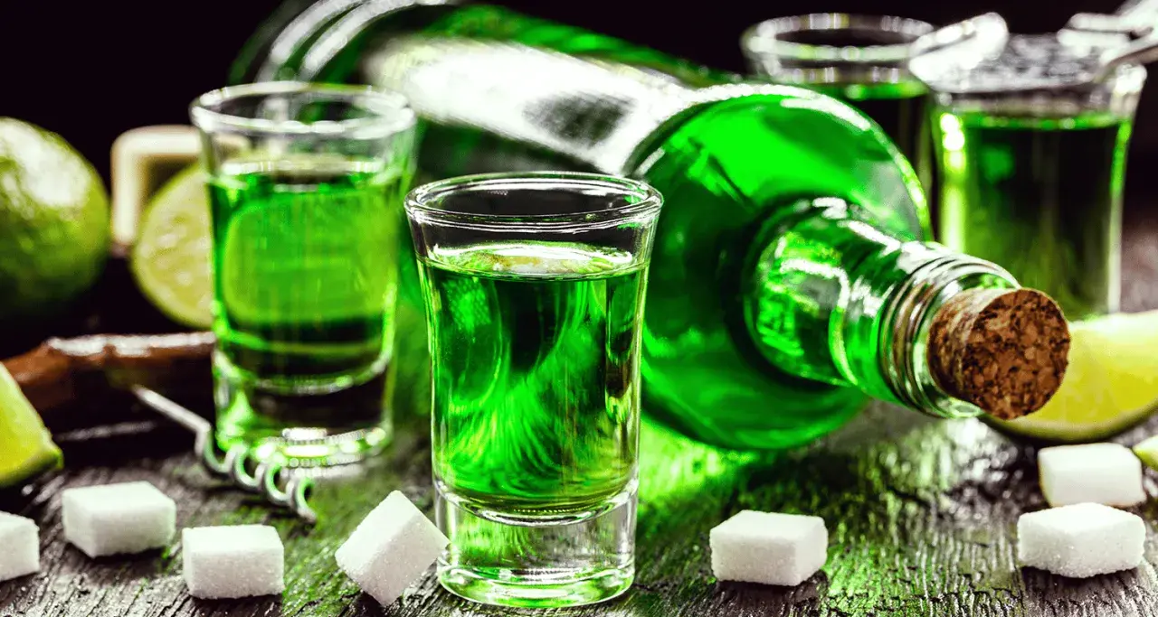 Grüner Branntwein aus Wermut, serviert in Schnapsgläsern mit Zuckerwürfeln und Limettenspalten.