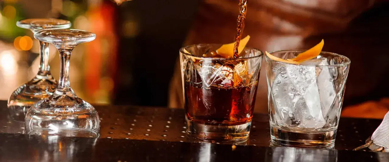 Ein dunkler Whisky wird in ein Glas mit Eis und Orangenzeste gegossen. So trinkt man Whisky.