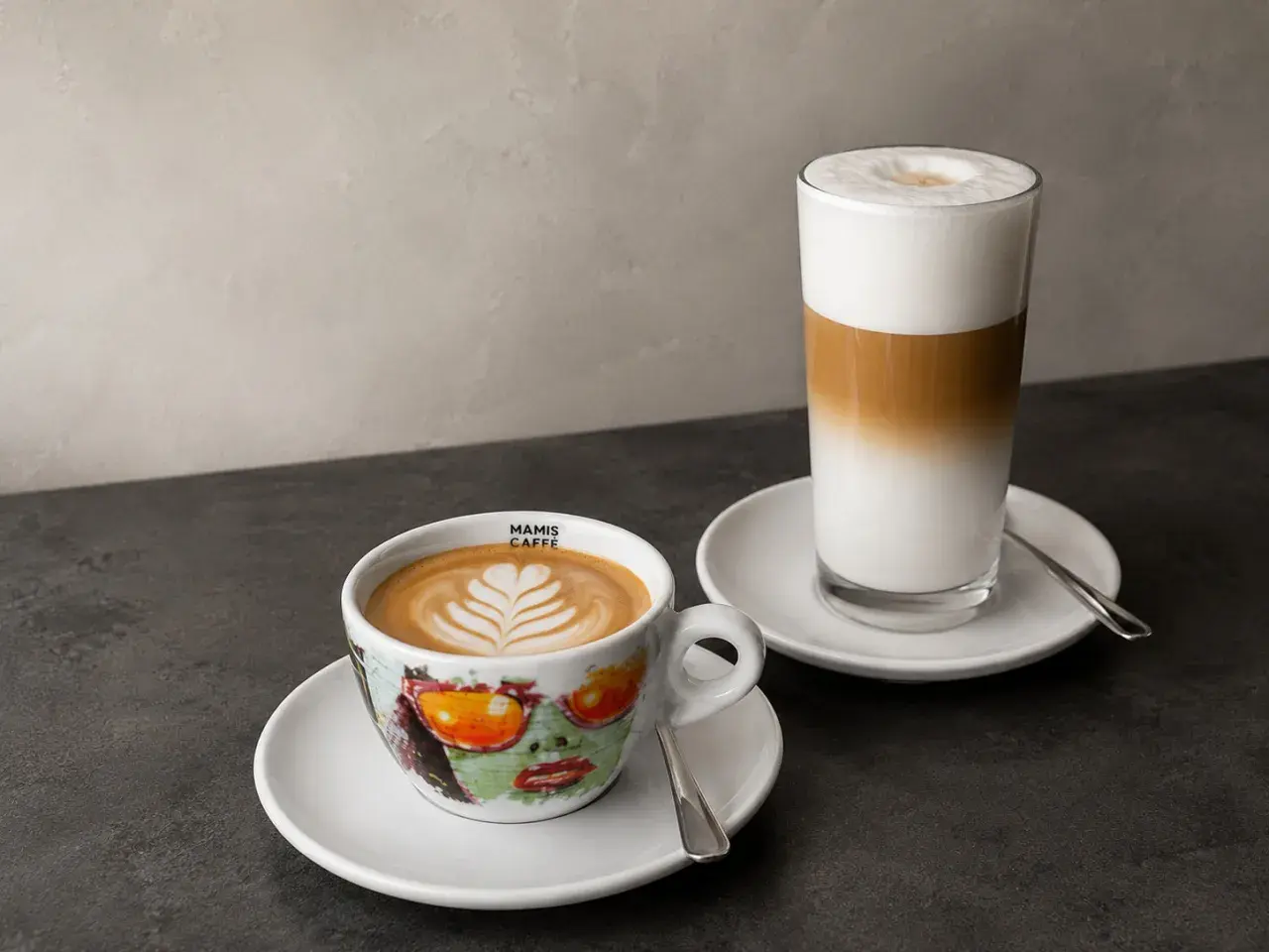 Zwei Kaffeespezialitäten: ein Cappuccino in einer bunten Tasse und ein Latte Macchiato im Glas. Die Frage "wie viel espresso in cappuccino" wird hier visuell beantwortet.