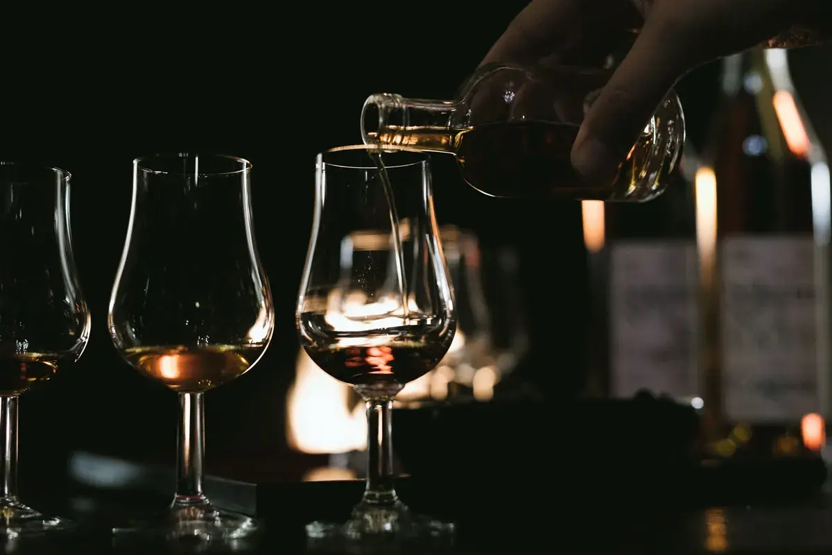 Ein Glas wird mit bernsteinfarbenem Brandy oder Cognac gefüllt, während andere Gläser bereitstehen.