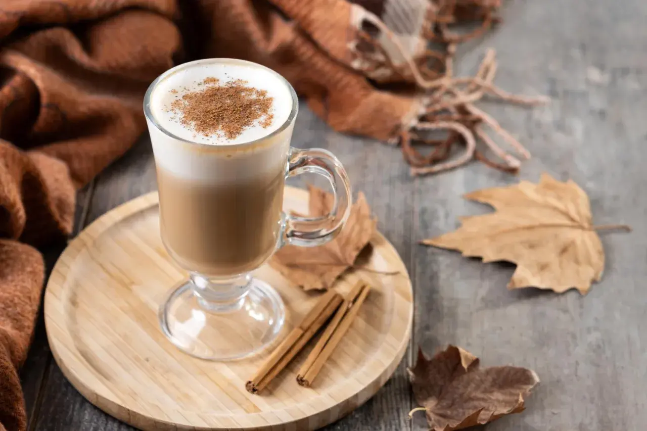 Ein warmer Herbst Kaffee mit Zimt, umgeben von Blättern und einer kuscheligen Decke.