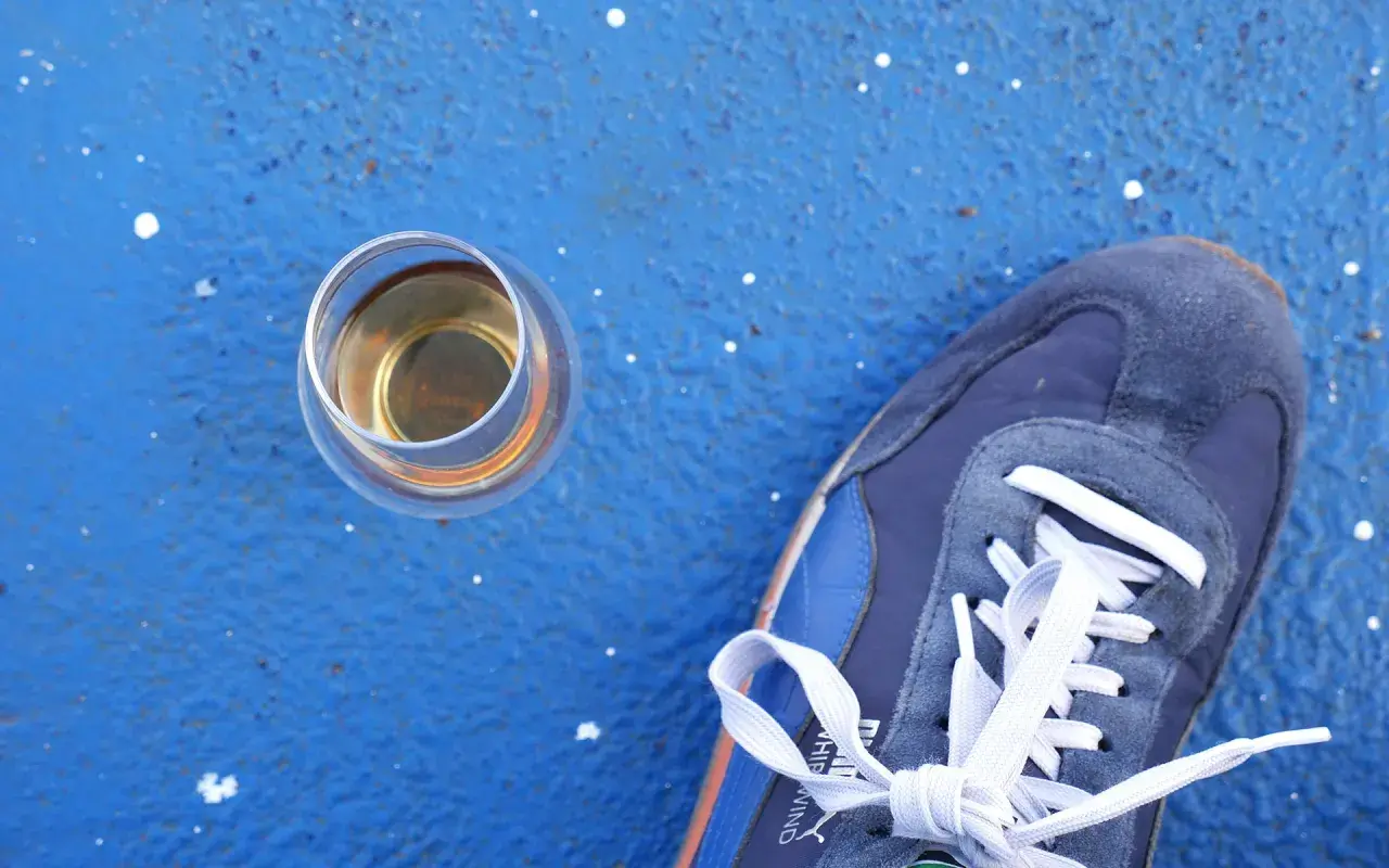 Ein Glas Whisky steht neben einem blauen Sneaker. Wer sich fragt, wie viel Kalorien hat Whisky, findet hier eine visuelle Anregung.